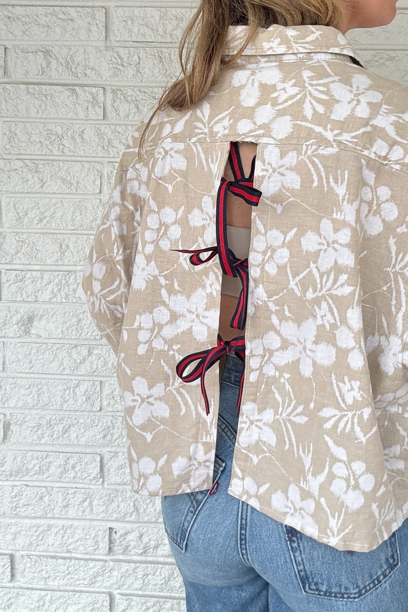 Front photo:
VonVie Harlow natural and white floral cropped button down shirt with relaxed elbow length sleeves

Back photo:
Back view of VonVie Harlow natural floral shirt with open back and red and navy ribbon ties