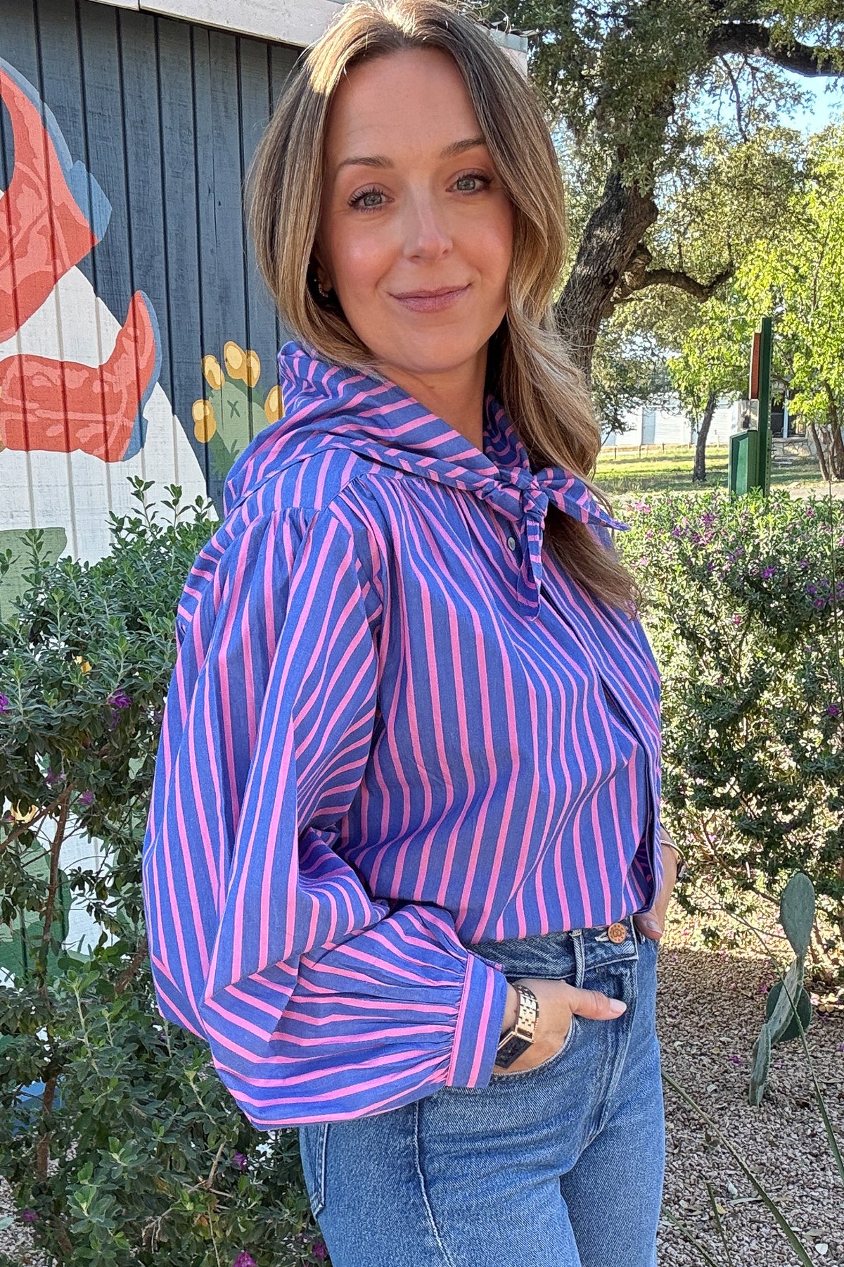 Women's blue and pink striped blouse with a matching tie-neck scarf, balloon sleeves, and button-front detail. Shop Cotton & Cashmere Boutique.