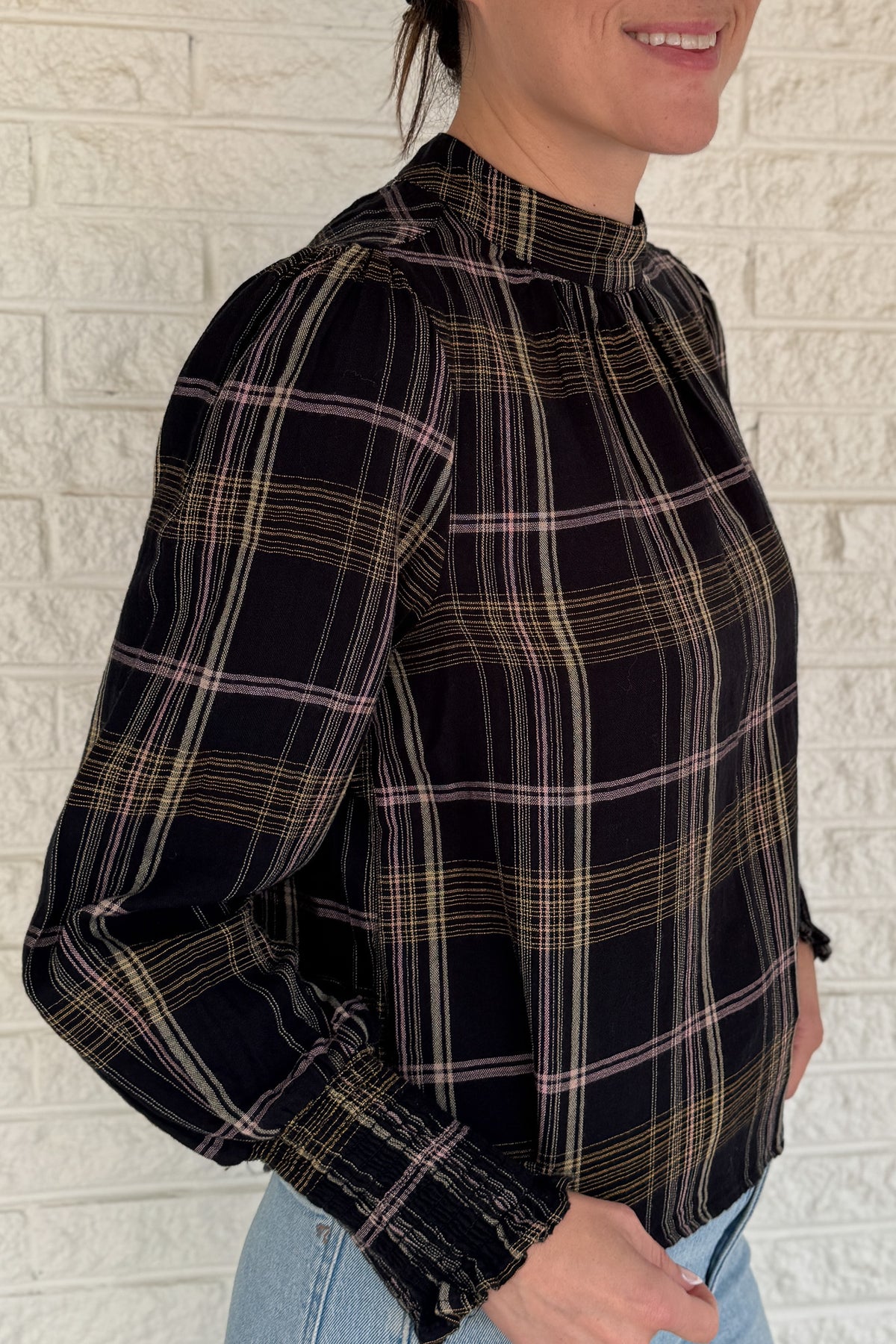 &nbsp;This plaid top blends classic style with feminine detail. Featuring a soft, lightweight drape, it buttons at the back of the neck for a clean finish. Smocked cuffs and subtle gathering at the neckline add texture and charm.