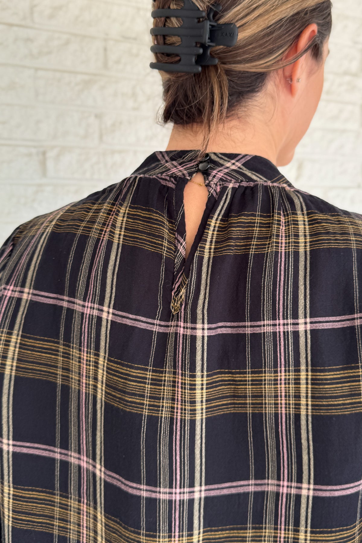&nbsp;This plaid top blends classic style with feminine detail. Featuring a soft, lightweight drape, it buttons at the back of the neck for a clean finish. Smocked cuffs and subtle gathering at the neckline add texture and charm.
