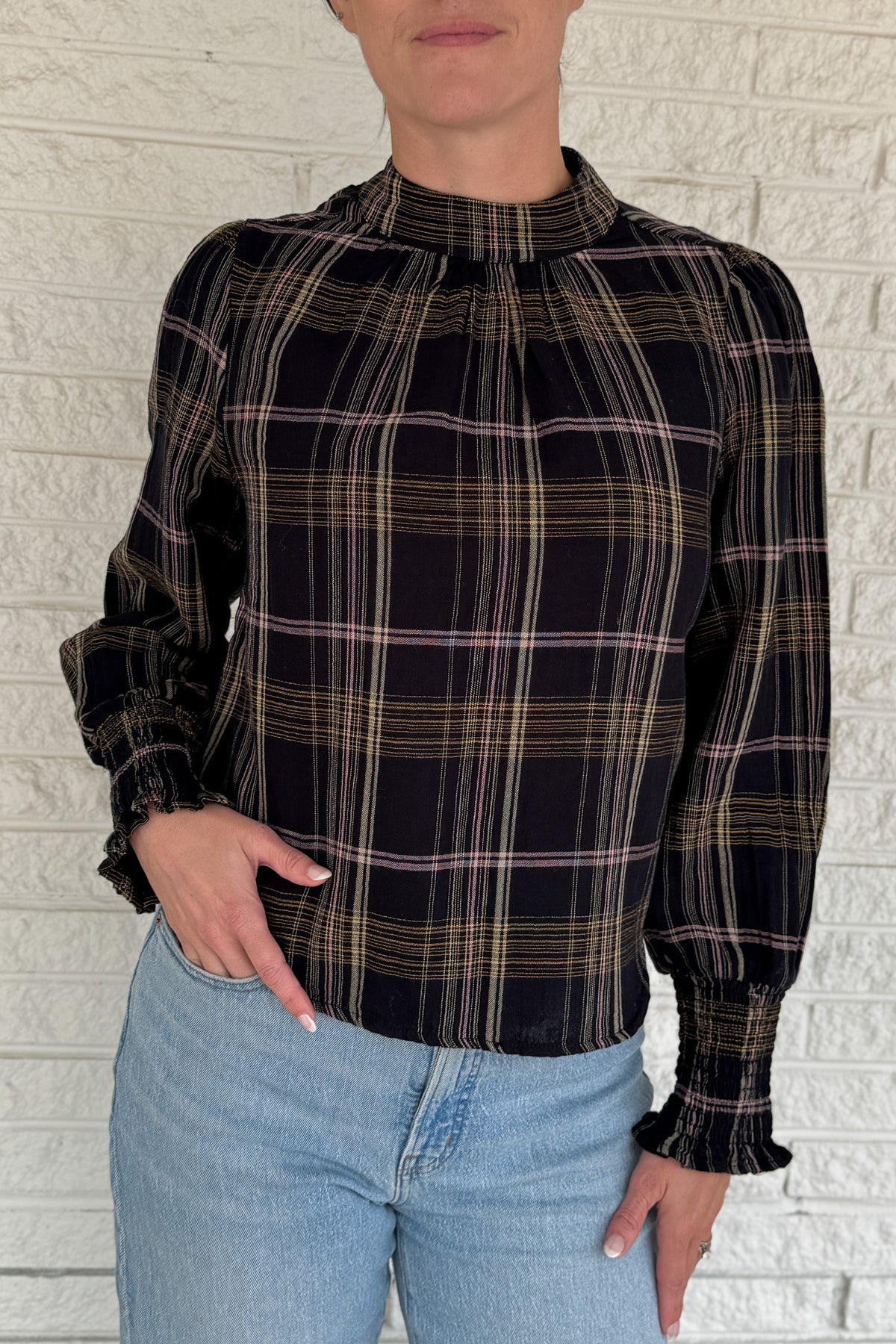 &nbsp;This plaid top blends classic style with feminine detail. Featuring a soft, lightweight drape, it buttons at the back of the neck for a clean finish. Smocked cuffs and subtle gathering at the neckline add texture and charm.