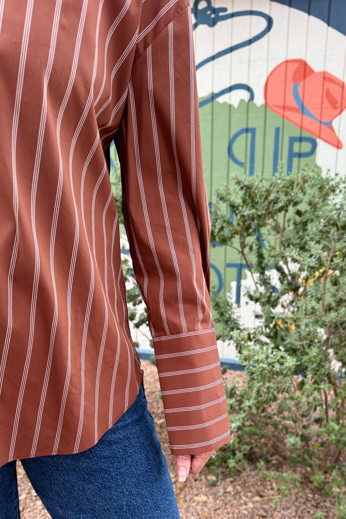 A rust striped button down top with an easy, relaxed fit and a unique lace up back detail. This women’s collared shirt features long sleeves, button cuffs, and an adjustable back that lets you create more shape at the waist. An effortless top to pair with jeans, trousers, or skirts for everyday wear.