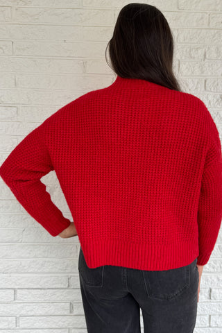 This bold red oversized sweater brings warmth and style together in one easy piece. Knitted in a soft, textured “square” weave, it features a cozy stand-up collar and ribbed finishes that keep the look clean and structured. Perfect for pairing with denim or a skirt for effortless everyday wear.