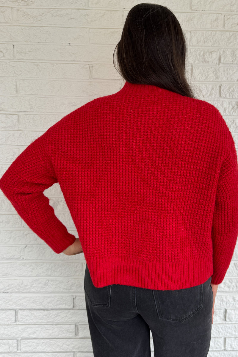 This bold red oversized sweater brings warmth and style together in one easy piece. Knitted in a soft, textured “square” weave, it features a cozy stand-up collar and ribbed finishes that keep the look clean and structured. Perfect for pairing with denim or a skirt for effortless everyday wear.