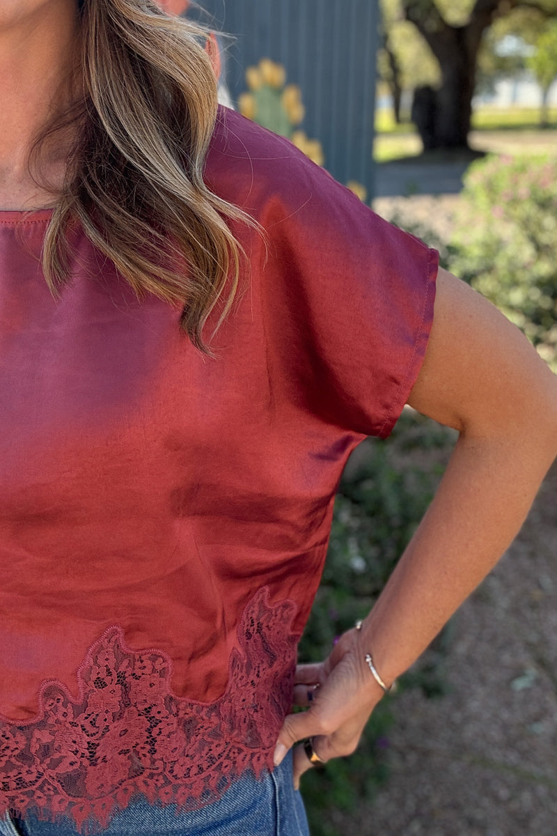 Feminine rose pink satin top featuring a soft sheen, round neckline, relaxed short sleeves, and intricate scalloped lace hem.