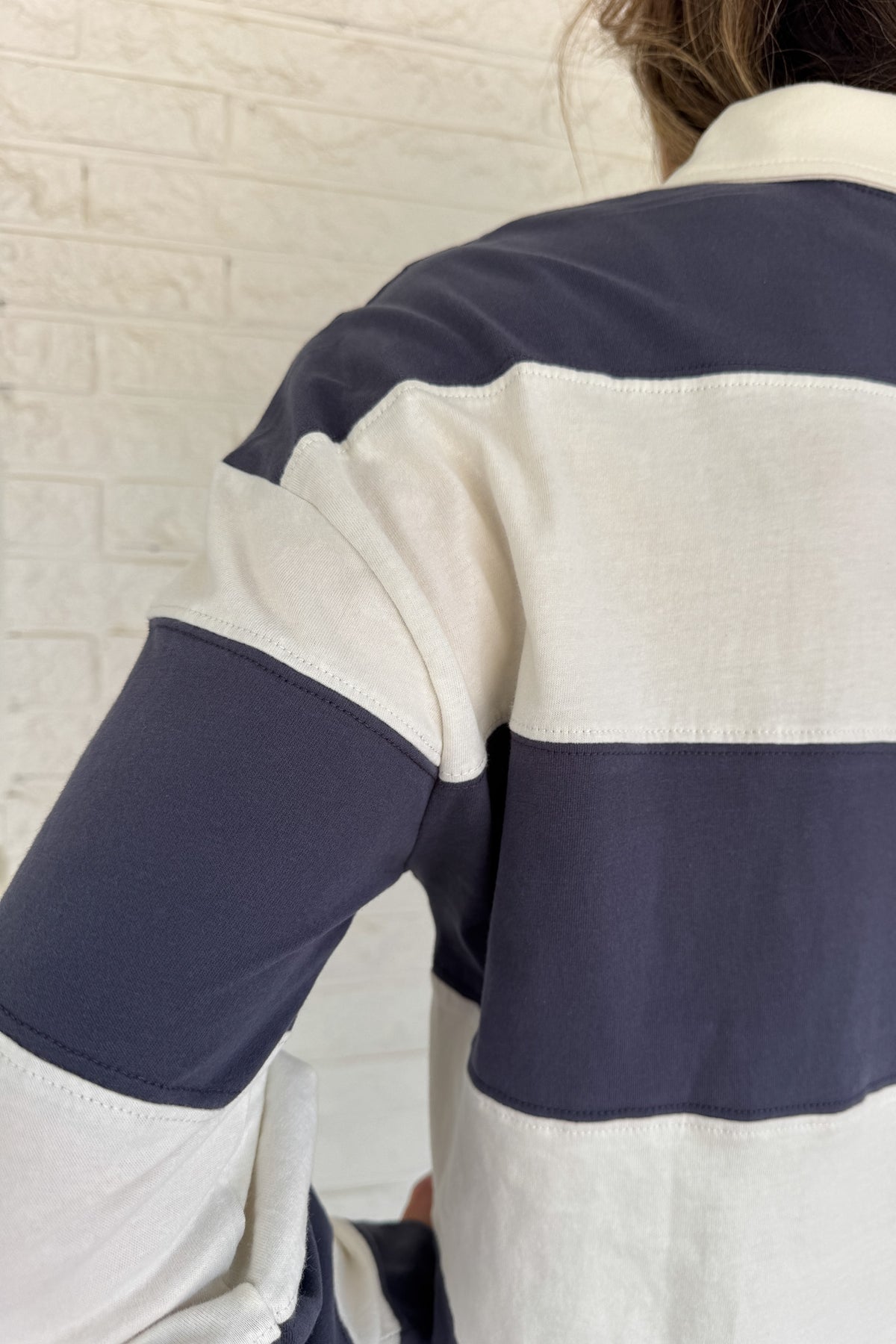 Sporty and timeless, this 100% cotton rugby-style top is a fresh take on a classic. Featuring wide navy and cream stripes with a button neckline, it’s an easy piece that blends casual comfort with effortless clothing style. Perfect for everyday wear — whether paired with denim or layered under a jacket.