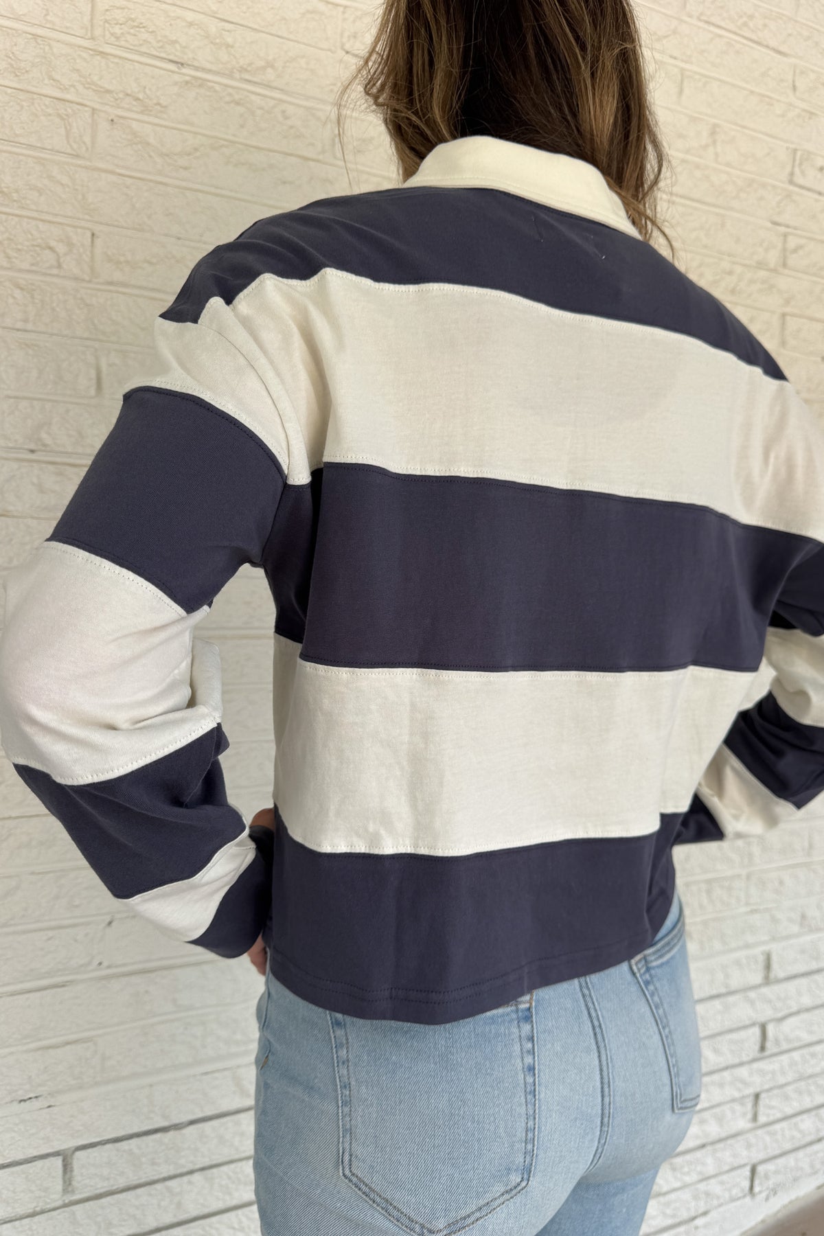 Sporty and timeless, this 100% cotton rugby-style top is a fresh take on a classic. Featuring wide navy and cream stripes with a button neckline, it’s an easy piece that blends casual comfort with effortless clothing style. Perfect for everyday wear — whether paired with denim or layered under a jacket.