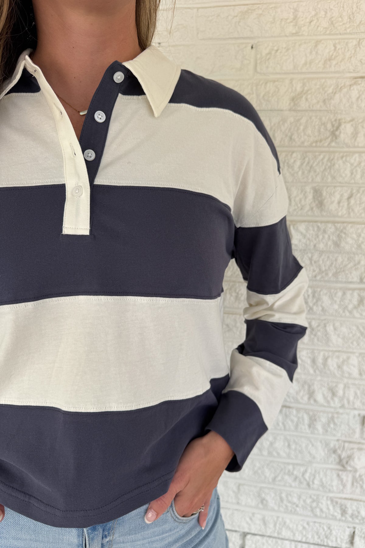 Sporty and timeless, this 100% cotton rugby-style top is a fresh take on a classic. Featuring wide navy and cream stripes with a button neckline, it’s an easy piece that blends casual comfort with effortless clothing style. Perfect for everyday wear — whether paired with denim or layered under a jacket.