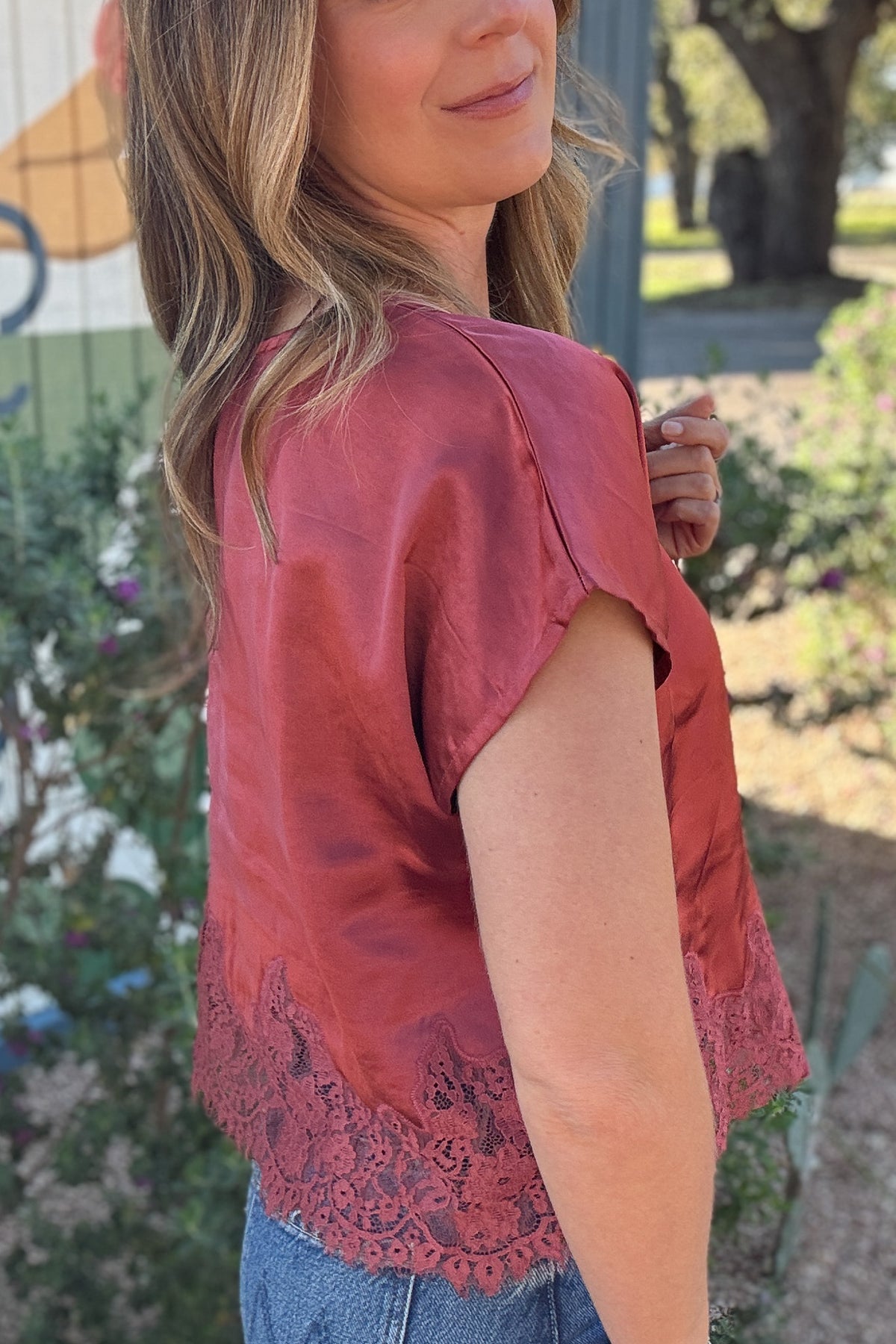 Women's mauve satin blouse with romantic floral lace detailing along the bottom, styled with blue denim for an effortless everyday look. Available at Cotton & Cashmere in Blanco, Texas.