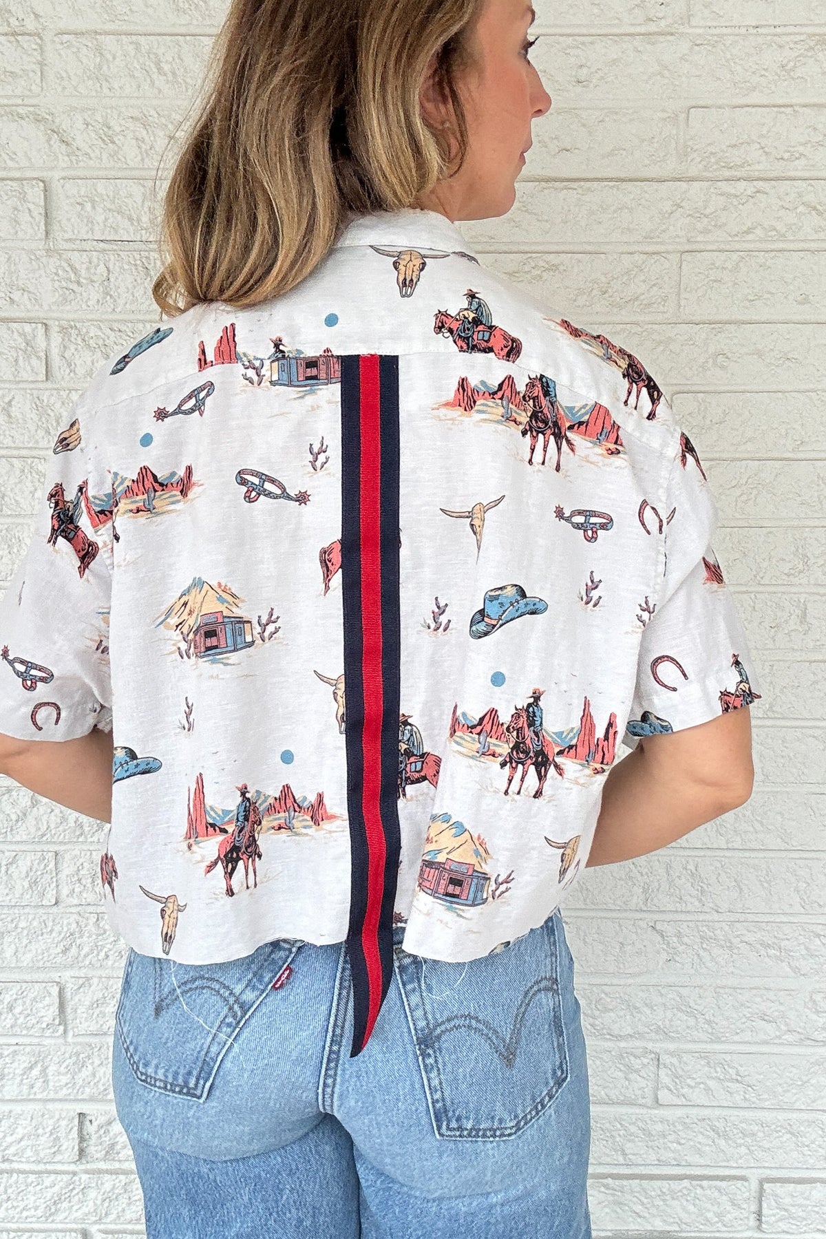 Front:
VonVie Stella Western print cropped button down shirt with short sleeves and raw hem

Back:
Back view of VonVie Stella Western print cropped shirt with red and navy ribbon detail
