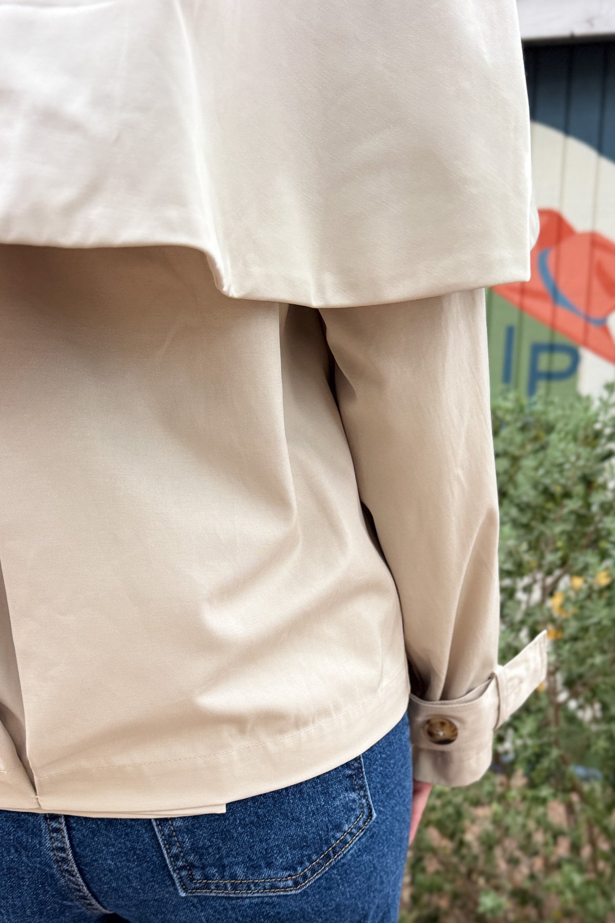 Women’s cropped beige trench coat with removable cape overlay, double-breasted buttons, wide lapels and cuff straps at Cotton & Cashmere in Blanco, Texas.
