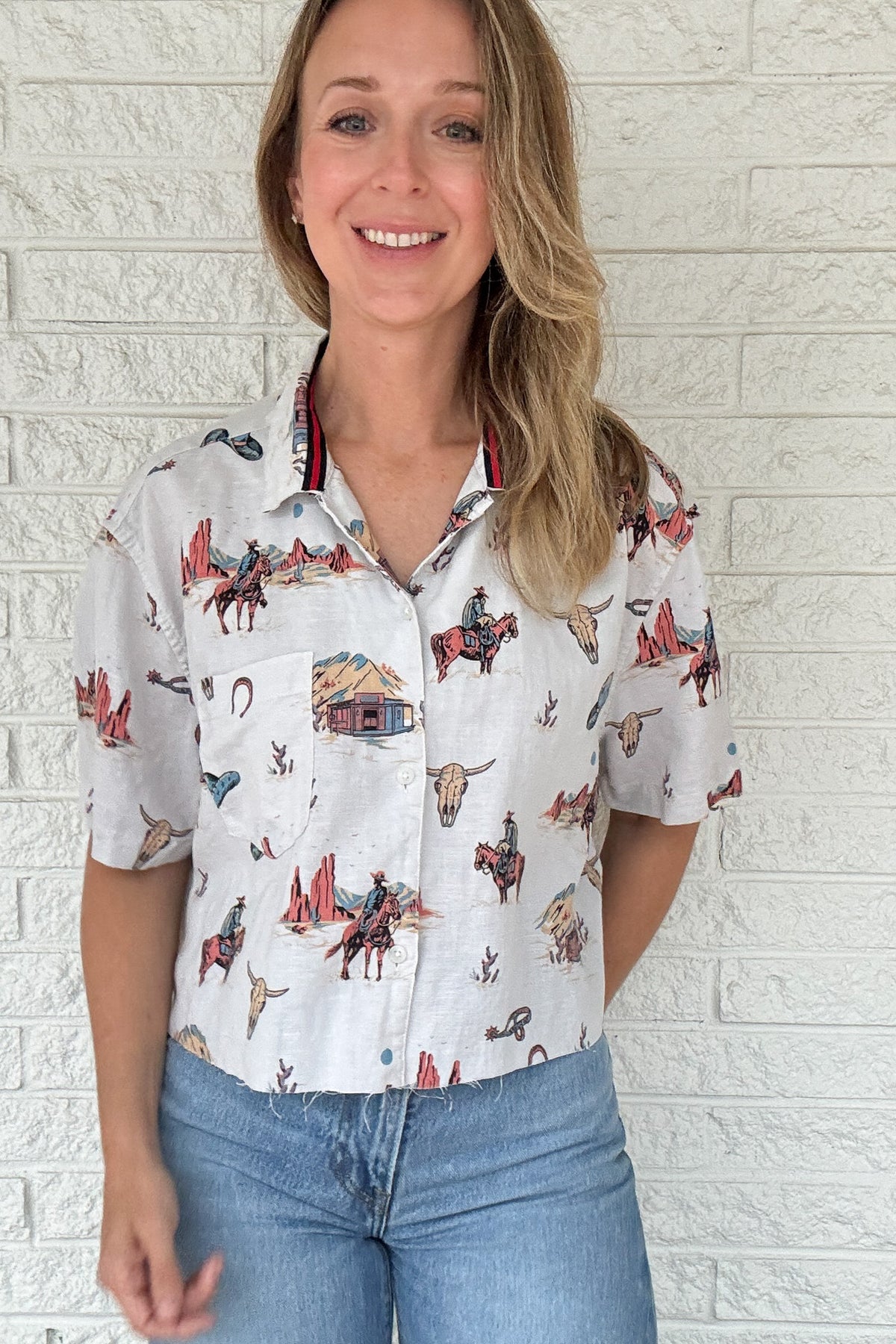 Front:
VonVie Stella Western print cropped button down shirt with short sleeves and raw hem

Back:
Back view of VonVie Stella Western print cropped shirt with red and navy ribbon detail