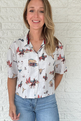 Front:
VonVie Stella Western print cropped button down shirt with short sleeves and raw hem

Back:
Back view of VonVie Stella Western print cropped shirt with red and navy ribbon detail