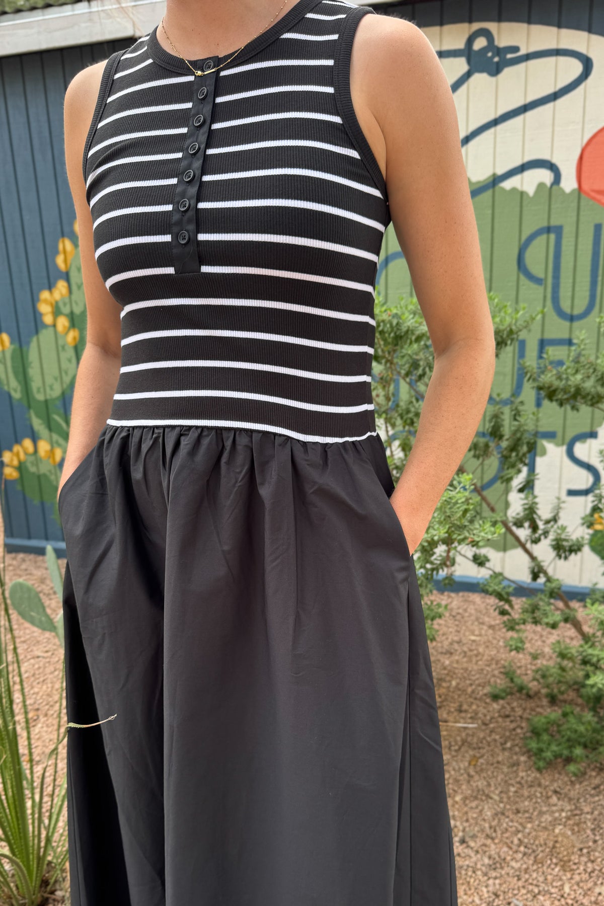 Close-up of a women’s black midi dress featuring a black and white striped ribbed bodice, round neckline and button placket.