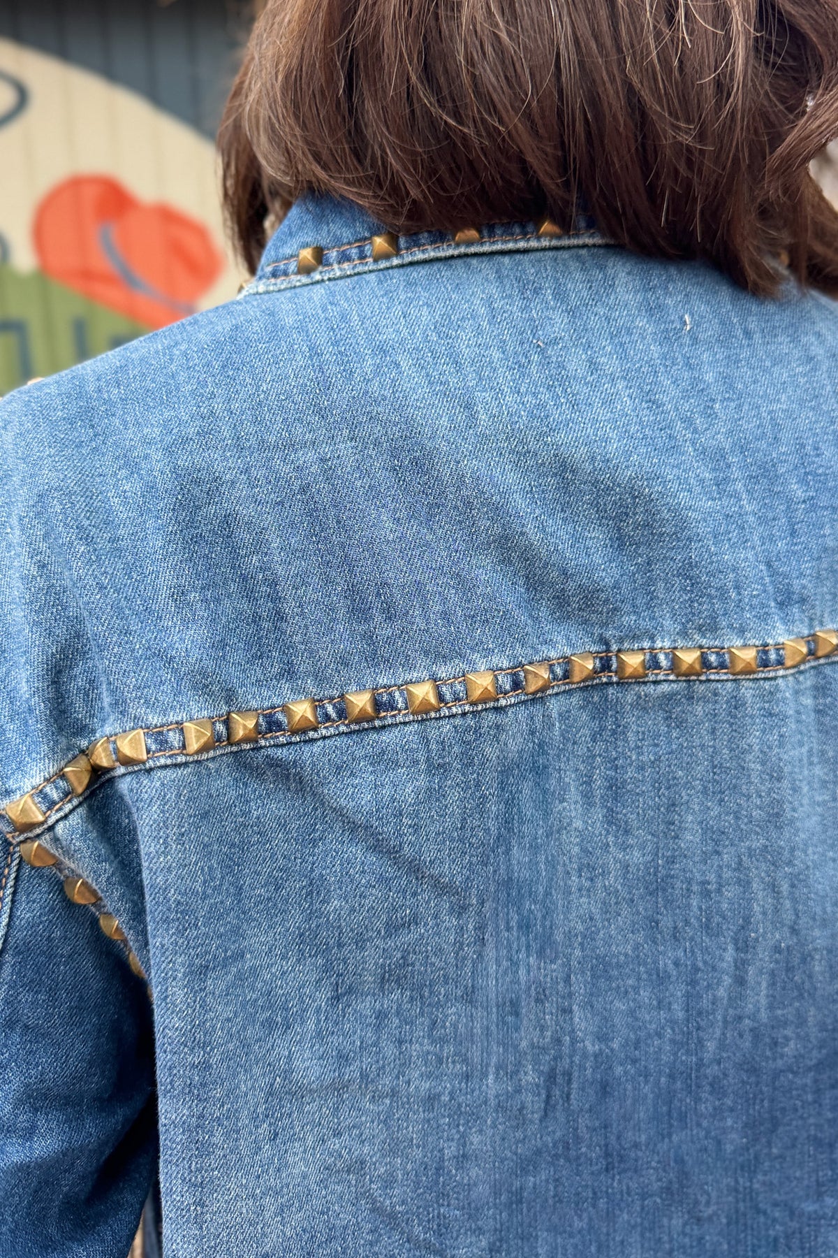 close up of women’s studded denim shirt jacket in medium wash with antique gold stud details, western-inspired seams and front patch pockets at Cotton & Cashmere in Blanco, Texas.