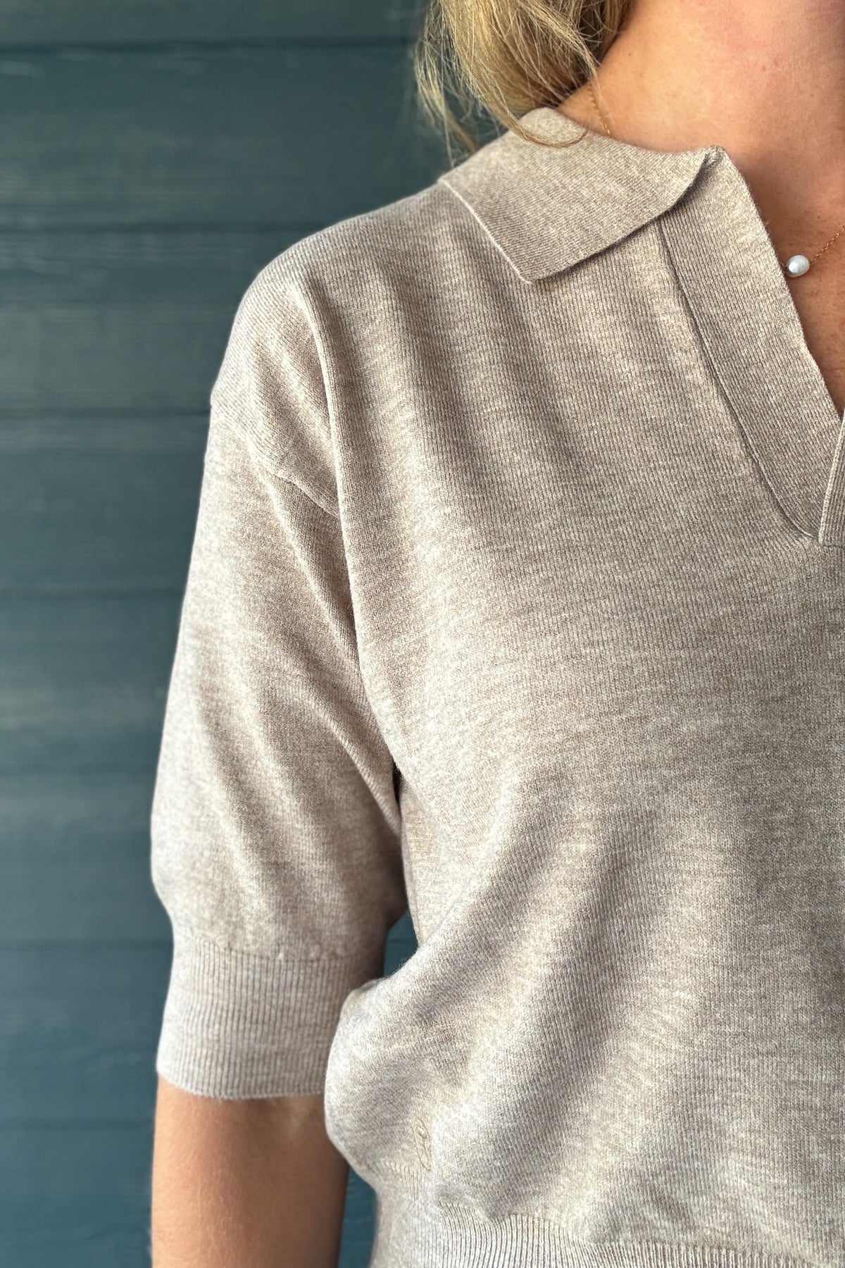 Close-up of taupe knit polo sweater showing the open V-neck collar, soft knit texture and ribbed short sleeves.
