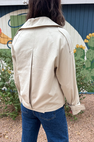 Women’s cropped beige trench coat with removable cape overlay, double-breasted buttons, wide lapels and cuff straps at Cotton & Cashmere in Blanco, Texas.