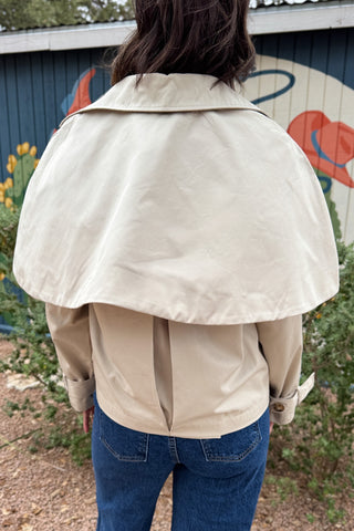 Women’s cropped beige trench coat with removable cape overlay, double-breasted buttons, wide lapels and cuff straps at Cotton & Cashmere in Blanco, Texas.