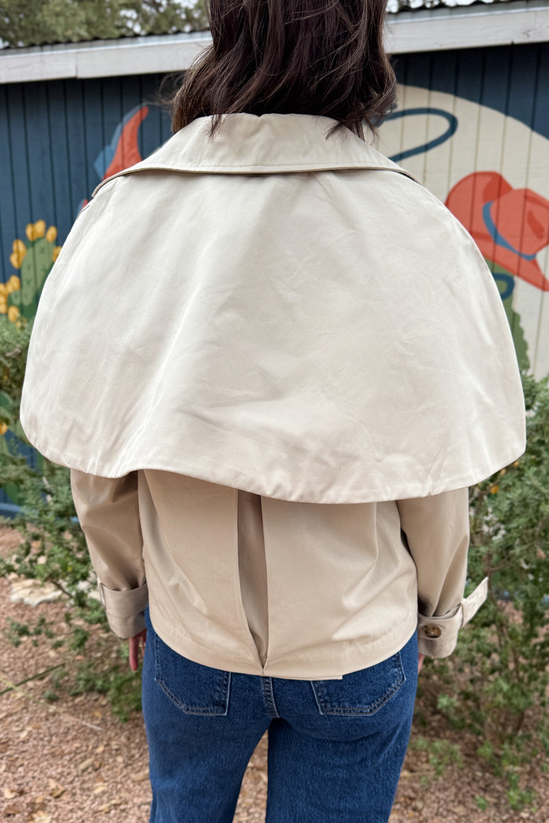 Women’s cropped beige trench coat with removable cape overlay, double-breasted buttons, wide lapels and cuff straps at Cotton & Cashmere in Blanco, Texas.