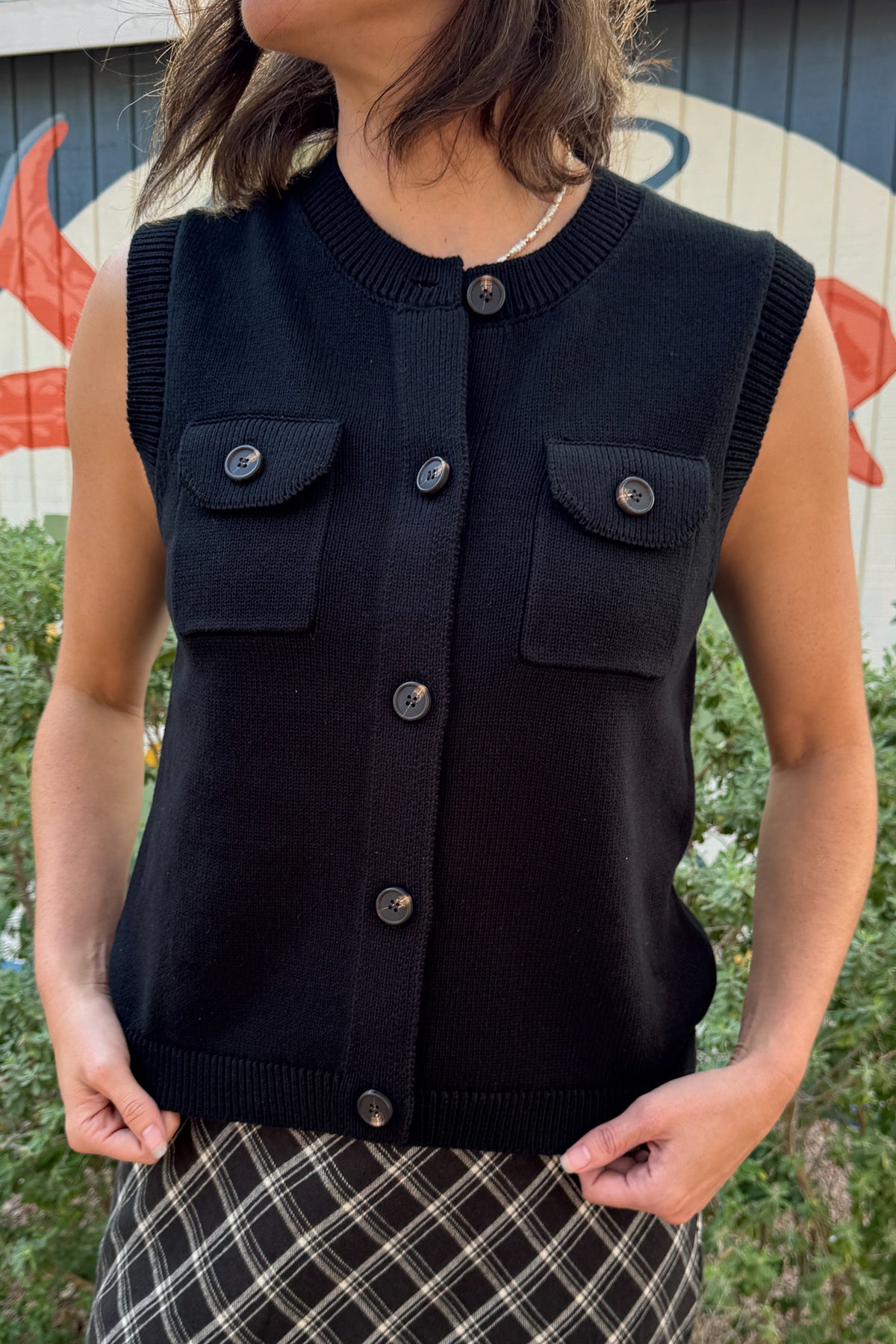 Women’s black 100% cotton sweater vest with button front, ribbed trim, and flap chest pockets.