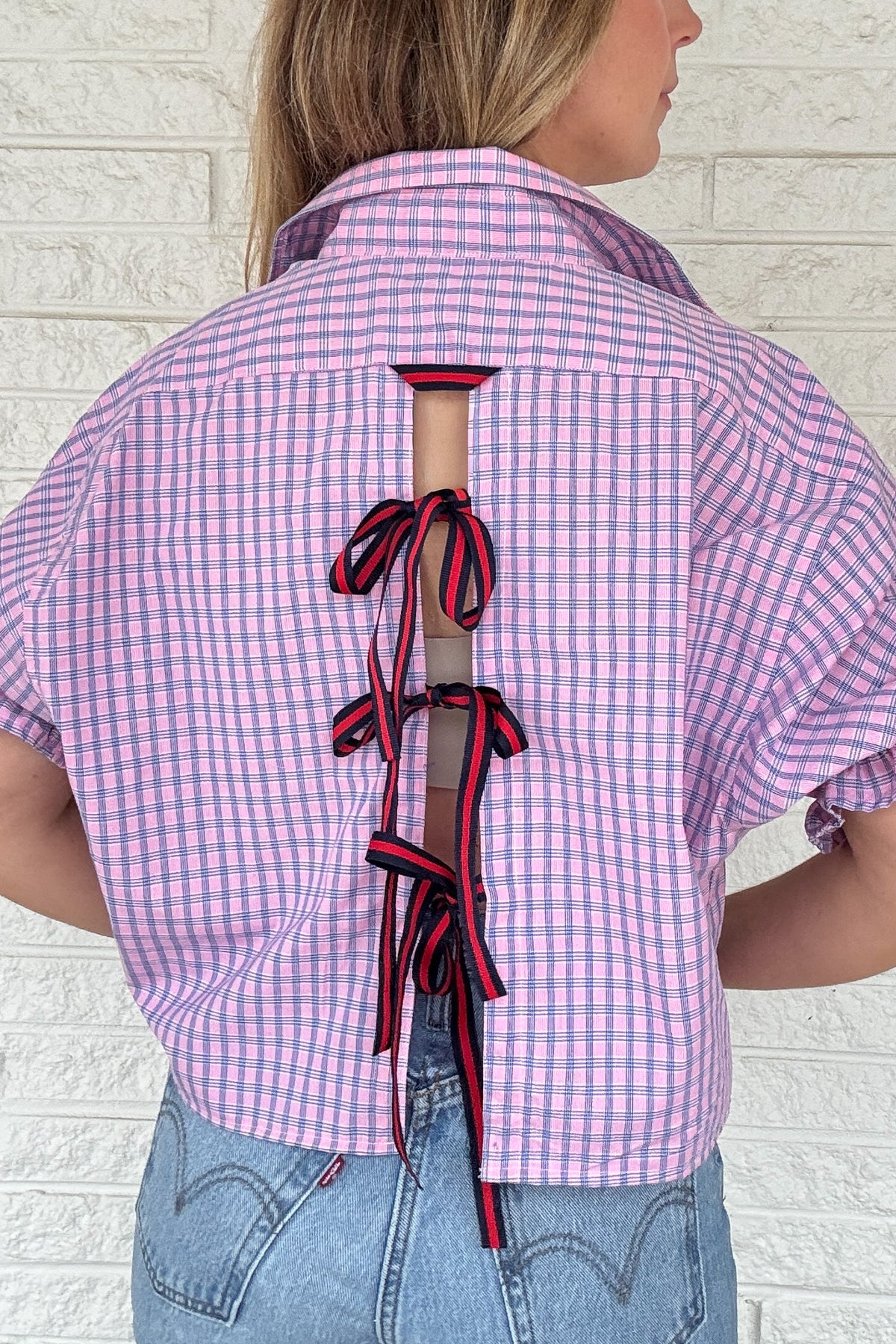 Front photo:
VonVie Harlow pink and blue plaid cropped button down shirt with puff sleeves and ruffled cuffs

Back photo:
Back view of VonVie Harlow pink and blue plaid shirt with open back and red and navy ribbon ties