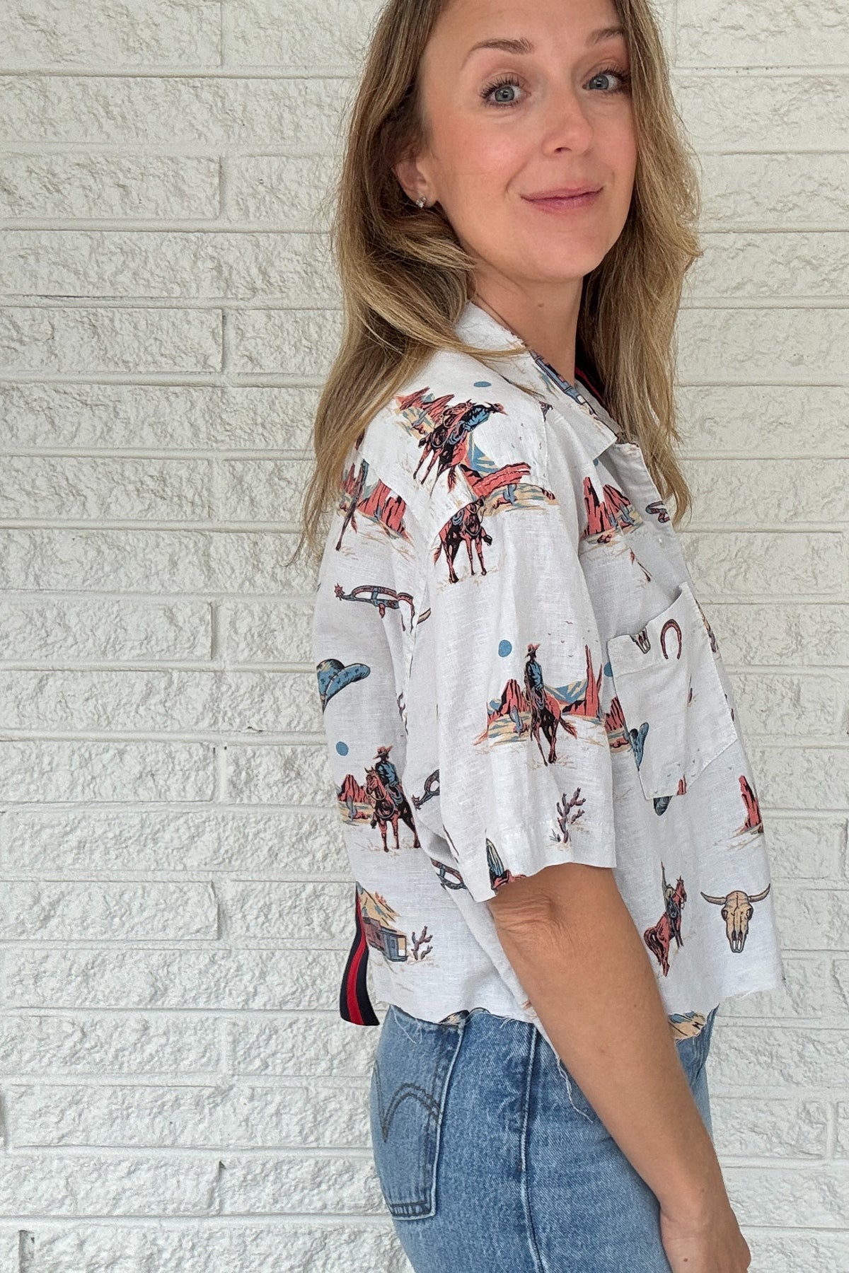Front:
VonVie Stella Western print cropped button down shirt with short sleeves and raw hem

Back:
Back view of VonVie Stella Western print cropped shirt with red and navy ribbon detail