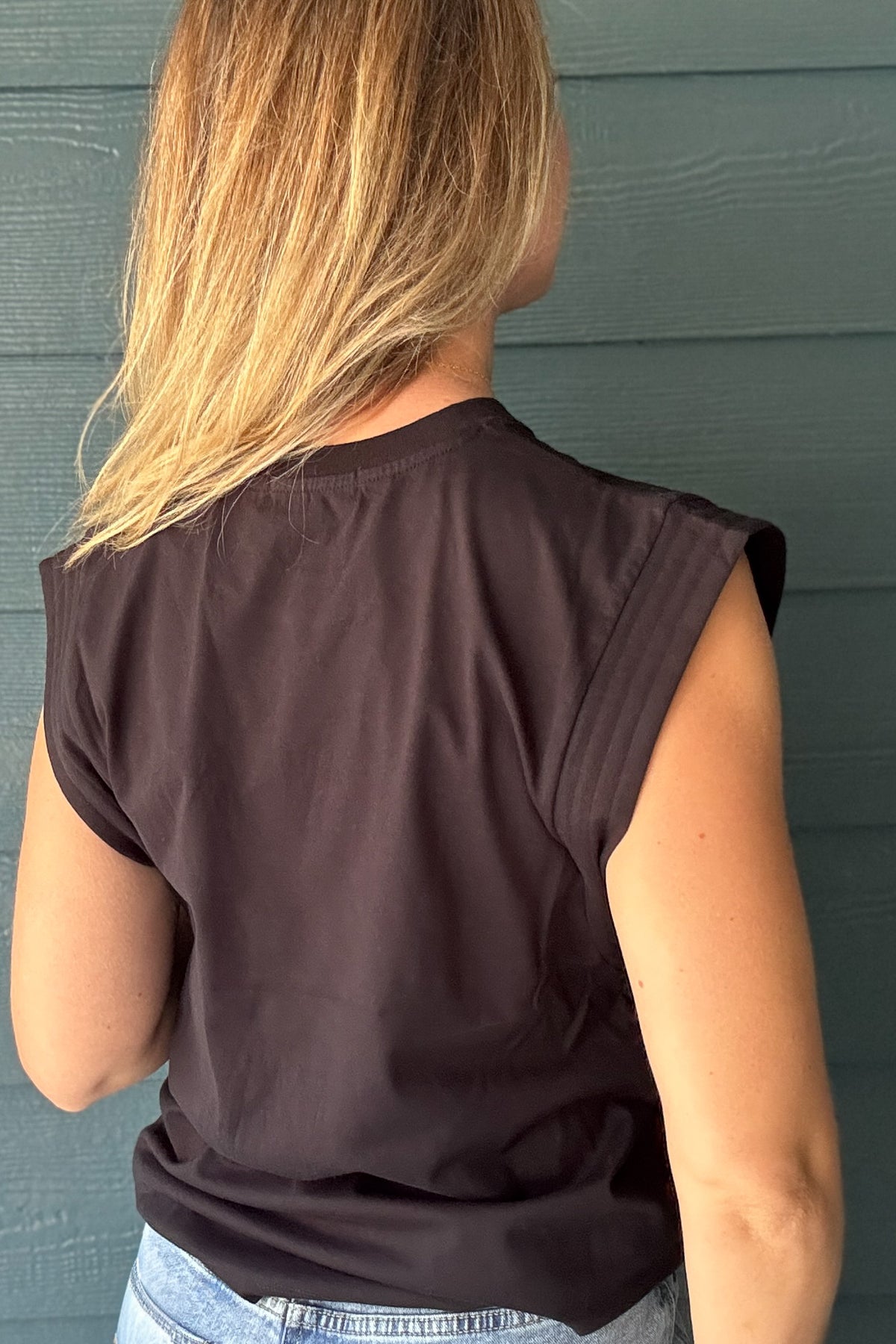 Back view of a women’s black sleeveless top with padded shoulders, a crew neckline and an easy draped silhouette.