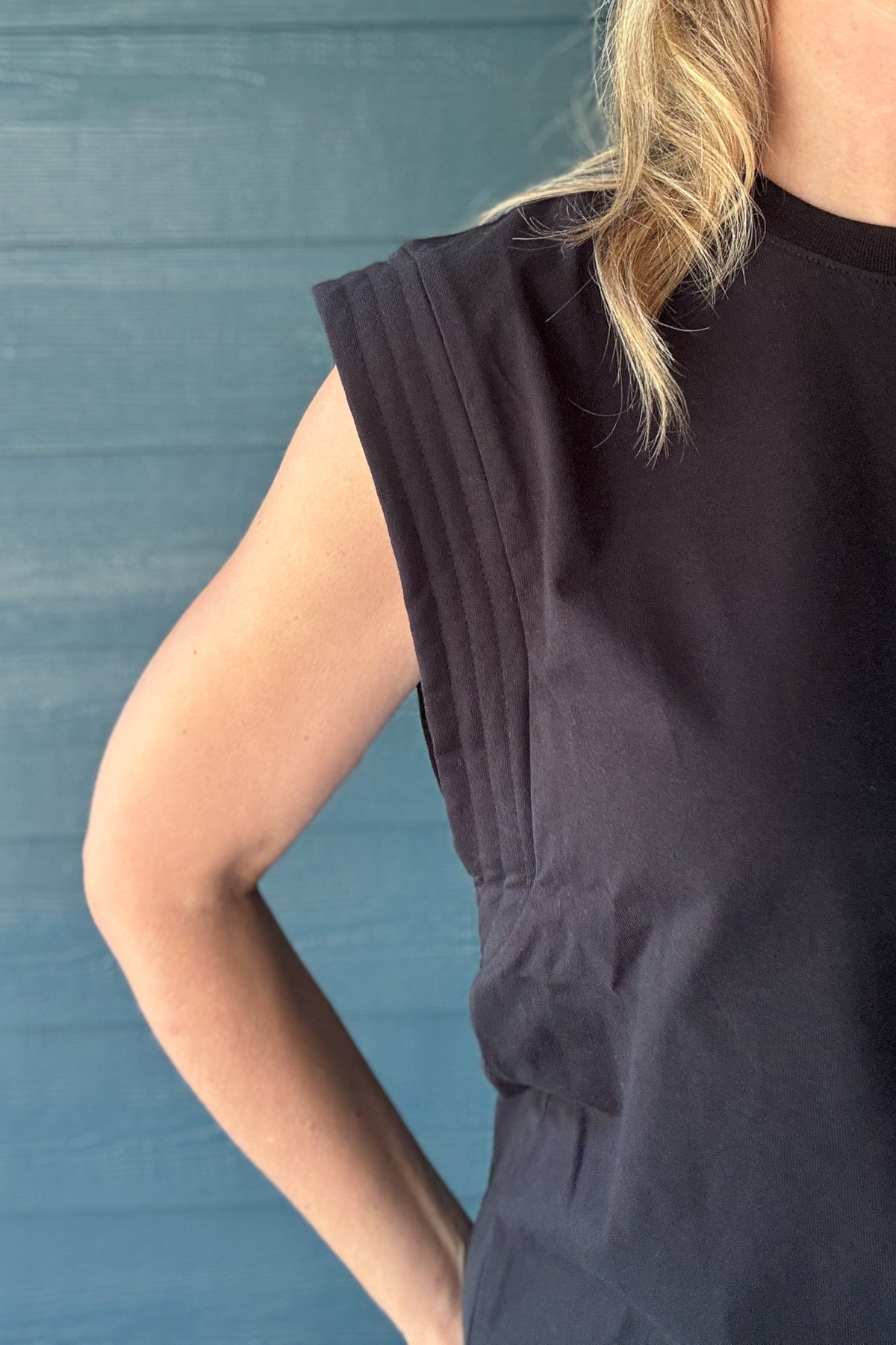 Close-up of a women’s black sleeveless top with structured padded shoulders, stitched detailing and a crew neckline.