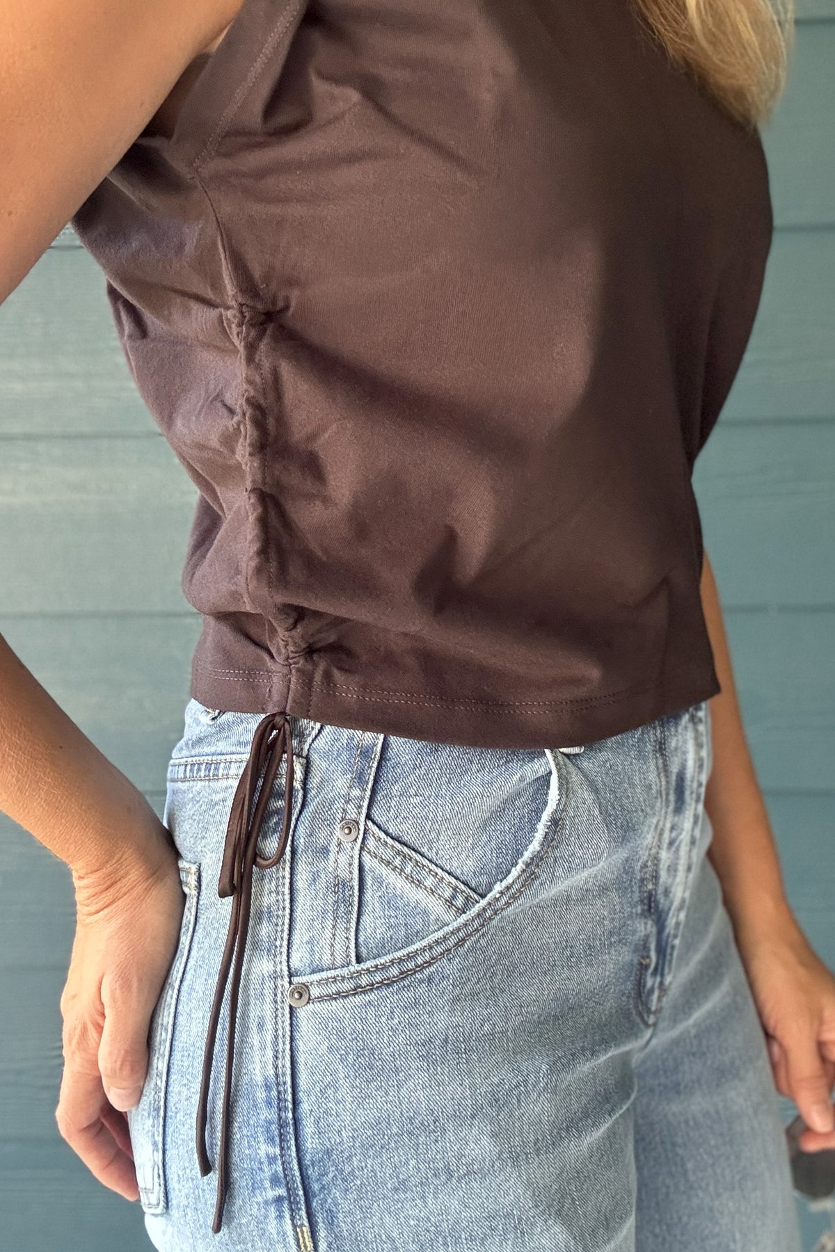 Side view of a women’s chocolate brown cropped top with adjustable drawstring ruching and a fitted sleeveless silhouette.