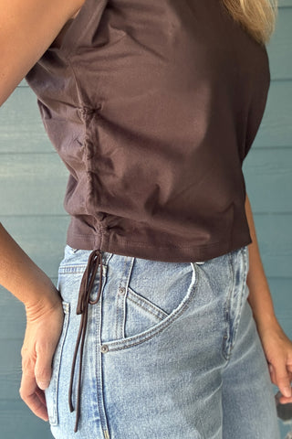 Side view of a women’s chocolate brown cropped top with adjustable drawstring ruching and a fitted sleeveless silhouette.