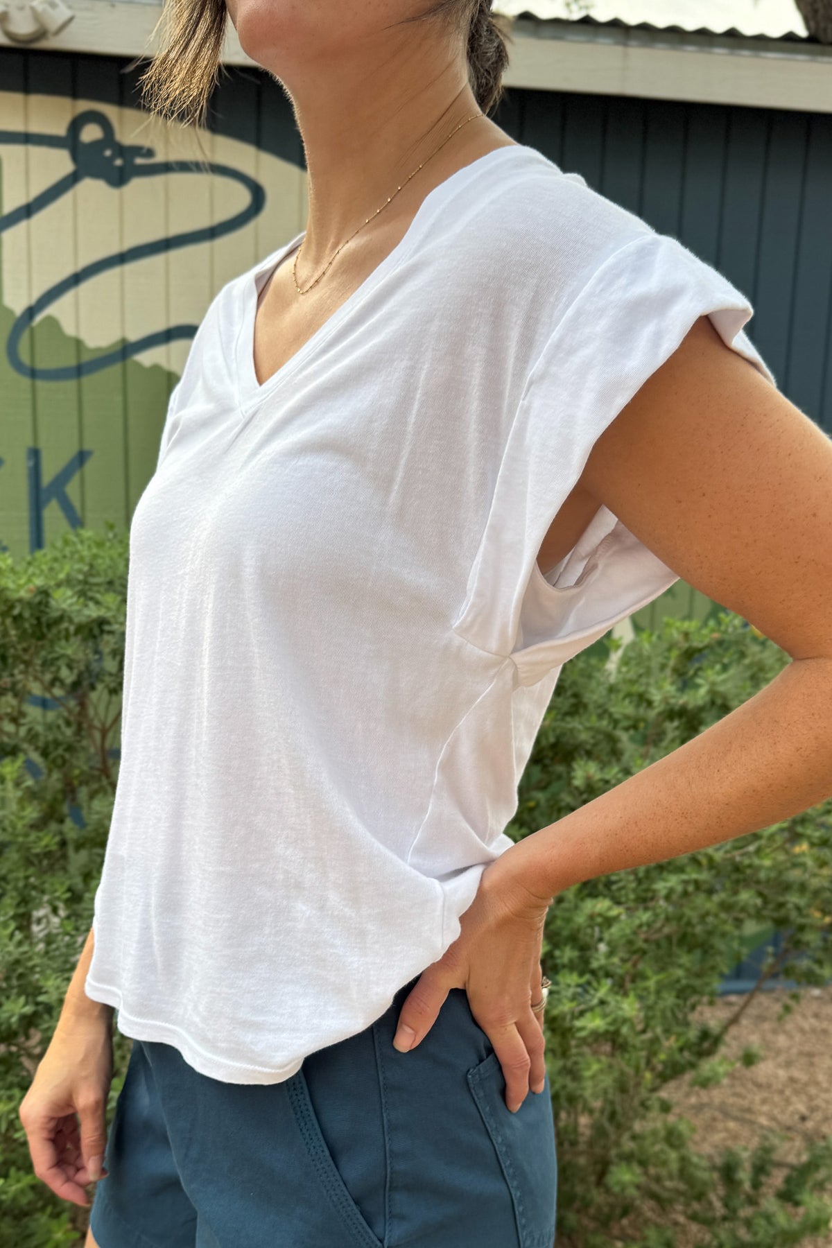 Women’s white V-neck top with wide cap sleeves, a relaxed fit and soft drape, styled with blue shorts at Cotton & Cashmere in Blanco, Texas.